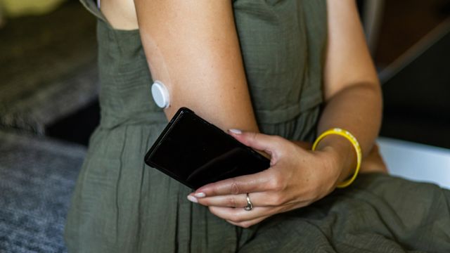 A woman checks a continuous blood glucose monitor attached to her upper arm using her phone. Having the flu can raise blood glucose levels, and diabetes requires extra attention to monitoring and management when sick.