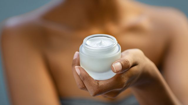 A woman holds a small jar of moisturizer. Moisturizing can help soothe psoriasis.