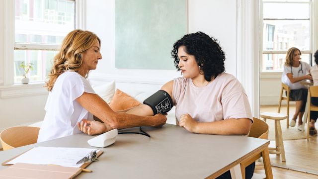 A healthcare provider takes a blood pressure reading for a woman during a healthcare appointment for obesity treatment.