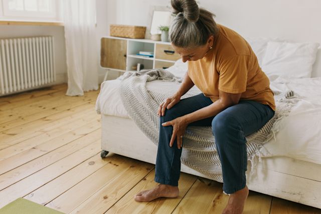 mature woman with knee pain sitting on bed