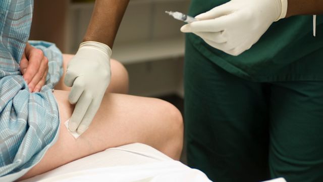 A healthcare provider cleans the injection site on the thigh of a woman who is being treated for cancer with subcutaneous immunotherapy.
