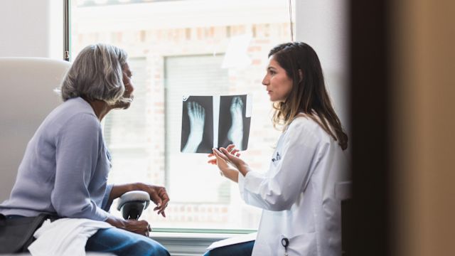 A healthcare provider discusses the results of a foot x-ray with a female patient who is managing diabetes. Diabetic peripheral neuropathy can cause damage to the structures of the foot.