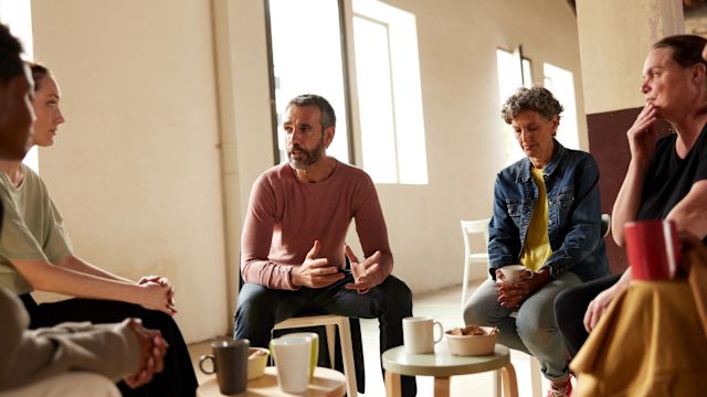 A group of adults gather at a support group for people who are caregivers to loved ones with cancer. Support groups can have benefits to both people living with NETs and caregivers.
