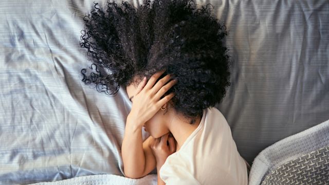 A young woman stays in bed during the middle of the day, recovering from a migraine attack.
