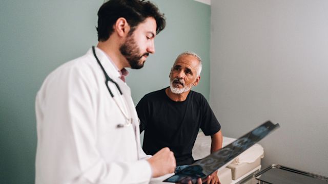 An oncologist reviews the results of an imaging test with a male patient who has been diagnosed with a neuroendocrine tumor (NET).