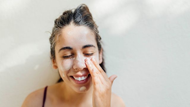 A young woman applies sunscreen to her face. Wearing sunscreen helps protect the skin from sun damage that could make atopic dermatitis symptoms worse.