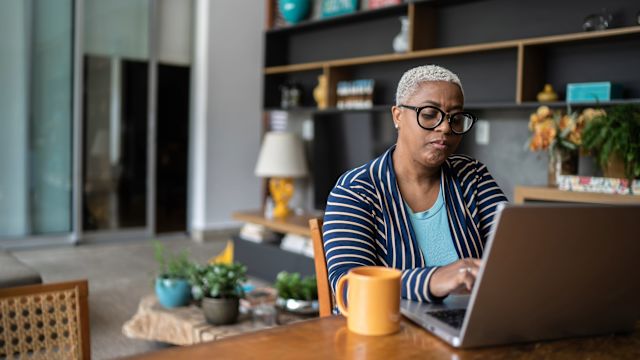 A woman researches MASLD and liver disease with a laptop. She is sitting in her home office and has a cup of coffee.