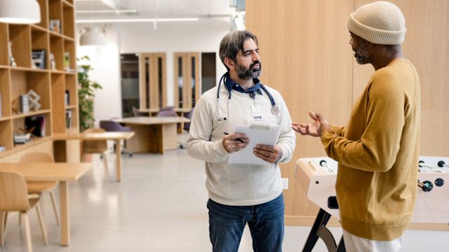 An adult man with epilepsy talks to his neurologist about the next steps in treatment in a common area of a medical clinic.