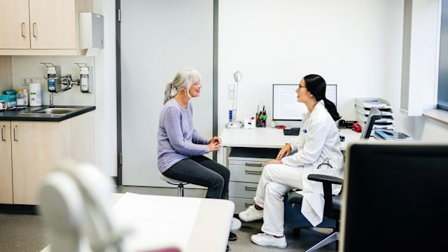 A senior woman and her oncologist discuss treatment options for melanoma in a healthcare office setting.