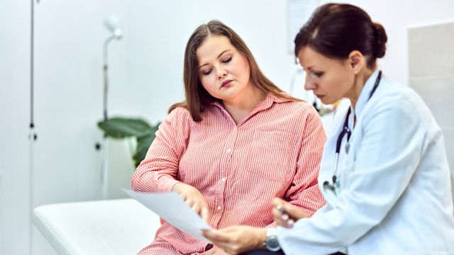 A woman with hypothalamic obesity discusses test result with her healthcare provider in an exam room.